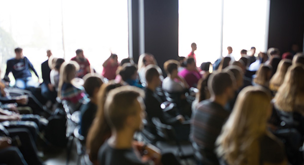 blurry photo of large group of people sitting in a conference room.